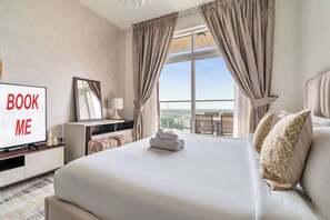 A hotel room with a bed, a TV, a desk, and a large window with curtains. - Free Housekeeping Visits During Your Stay - Stayshort - Cozy Studio in Arjan That Sleeps 2 (Dubai)