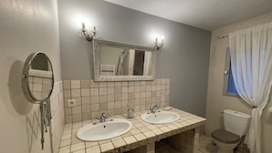 Une salle de bain avec deux lavabos, un miroir, des toilettes et un rideau de douche.