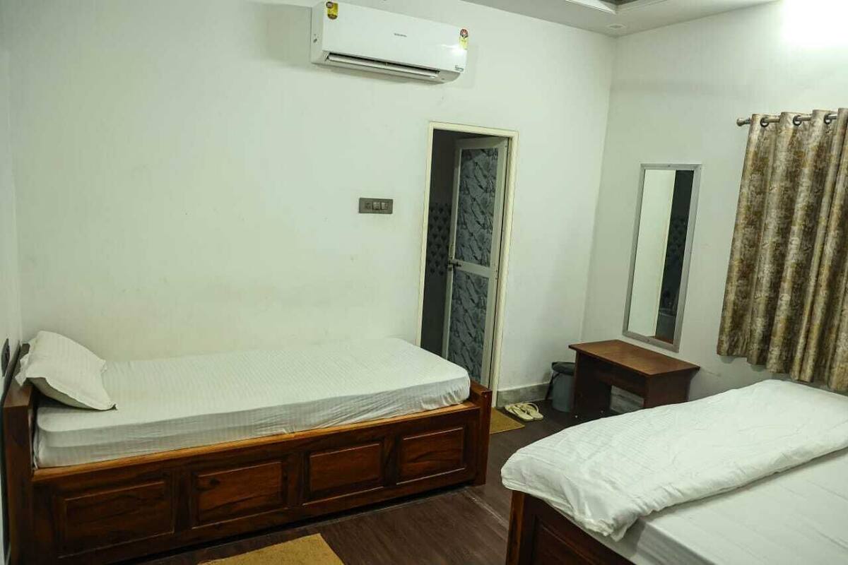 A bedroom with two wooden beds, an air conditioner, a small wooden table, a mirror, and a curtain.