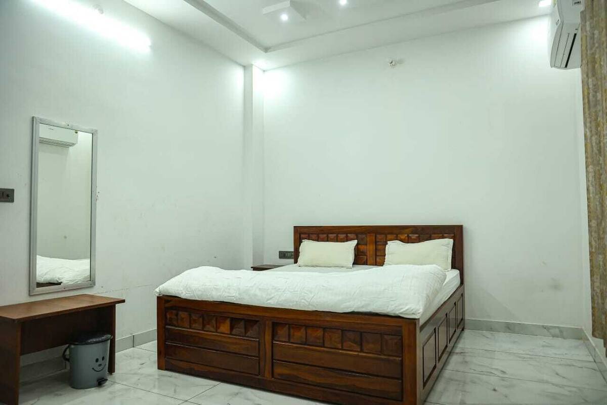A bedroom with a wooden bed, a small bedside table, a mirror, and a trash bin.