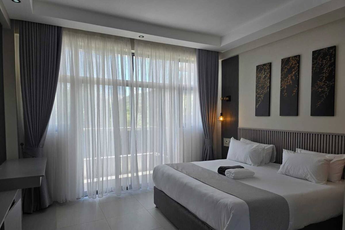 Habitación de hotel moderna con una cama grande, un escritorio y vistas a través de cortinas translúcidas.