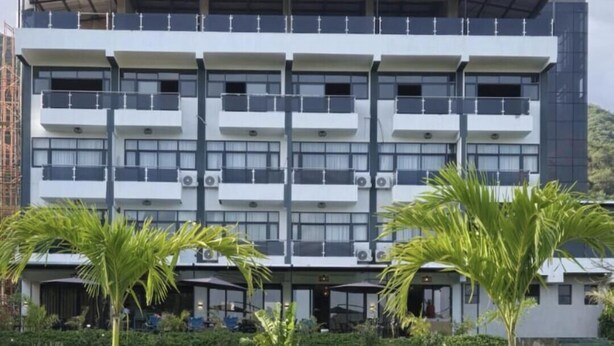 A multi-story hotel with balconies, a garden with palm trees and flowers, and a clear sky. - OLOISIRI NAMANGA HOTEL (Namanga)