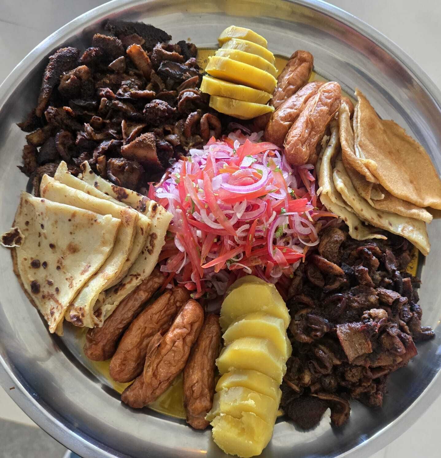 Une assiette contenant divers aliments, notamment de la viande, des pommes de terre et des légumes marinés.