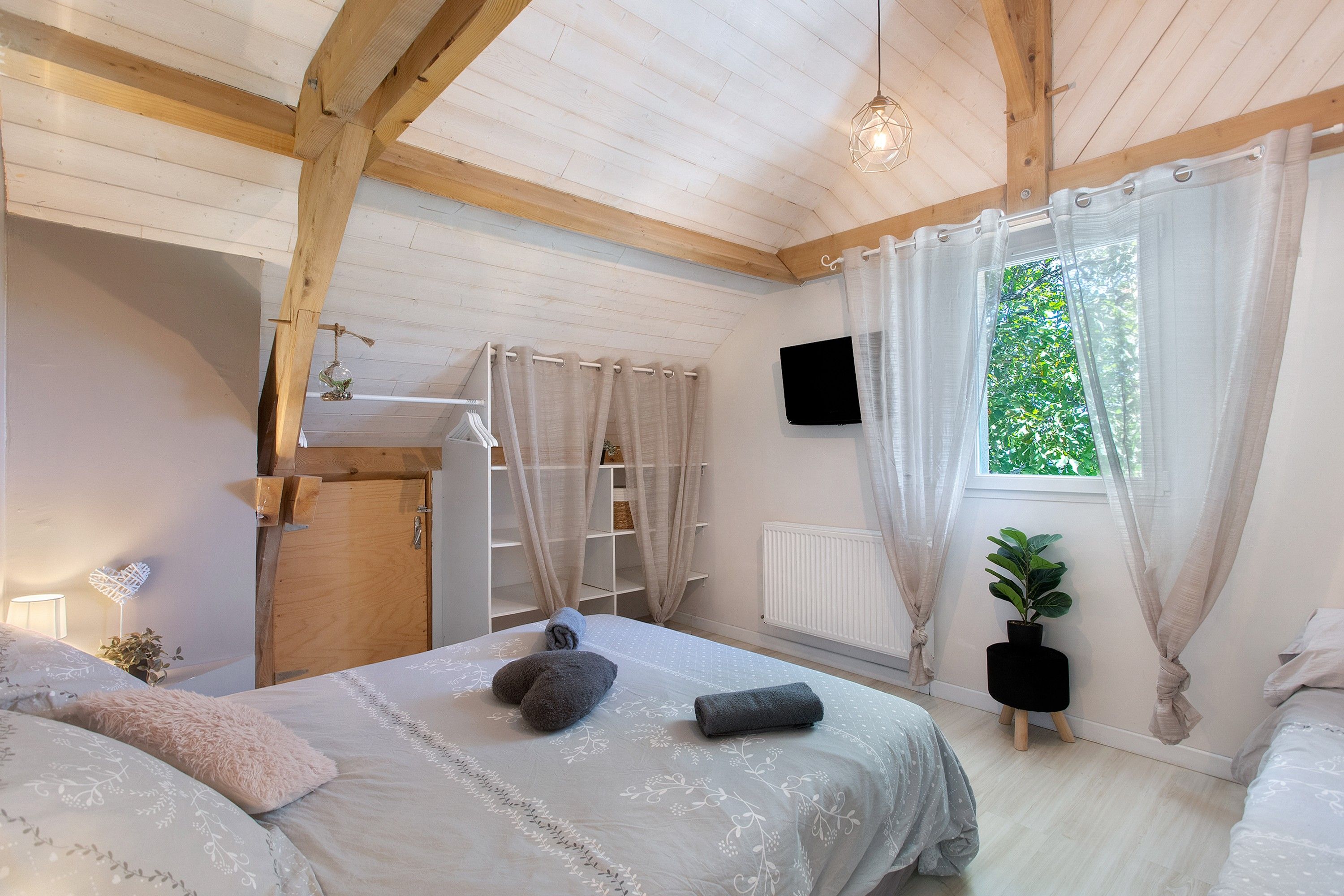 Ein Schlafzimmer mit Bett, einem Fenster mit Vorhängen, einer Heizung und einer kleinen Pflanze.