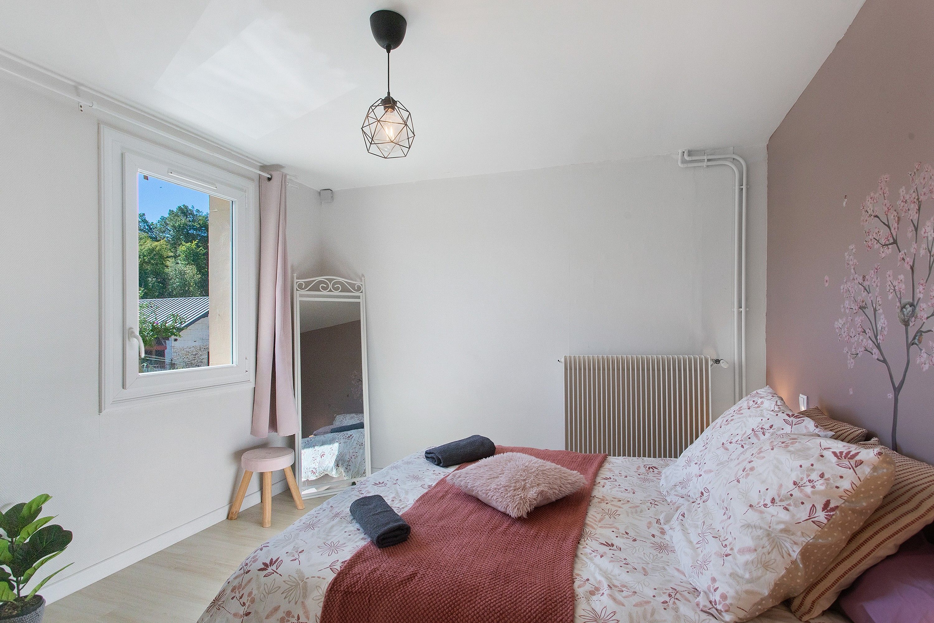A bedroom with a bed, a radiator, a window, and a plant.