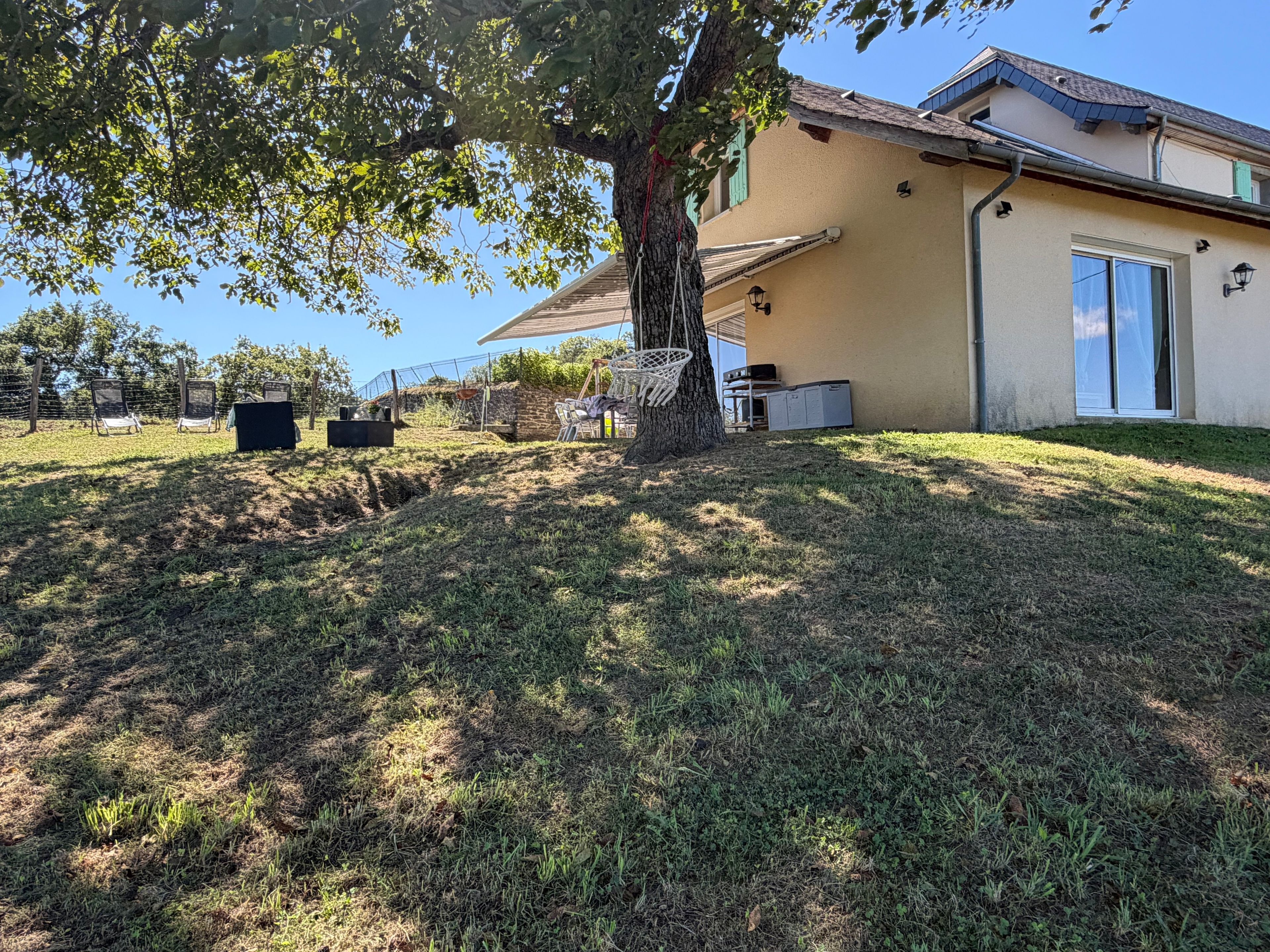 A residential property with a grassy yard, a tree, outdoor furniture, and a building with a sloped roof.