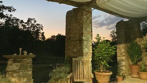 Un pilar de piedra, un banco de madera y plantas en macetas bajo una pérgola.