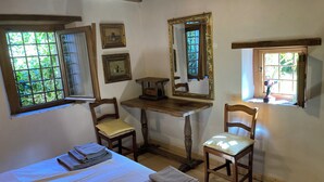 Una habitación con una cama, dos sillas, una mesa de madera, un espejo y cuadros en la pared.