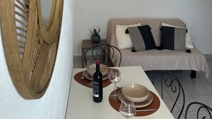 Een kamer met een eettafel gedekt voor twee personen, een bank, een spiegel en een kleine pot met een plantje.