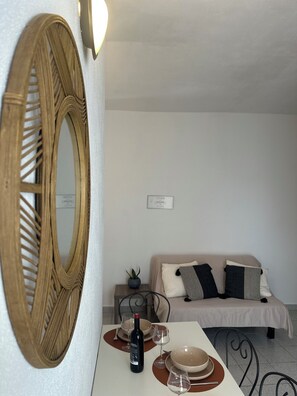 Ein Zimmer mit Esstisch, gedecktem für zwei Personen, einer Couch, einem Spiegel und einem kleinen Topf mit Pflanze.