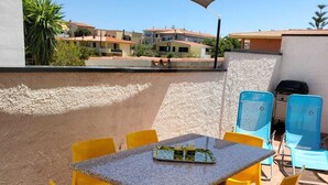 Een terras buiten met een stenen tafel en gele stoelen, een zwembad en een uitzicht op gebouwen in de verte.