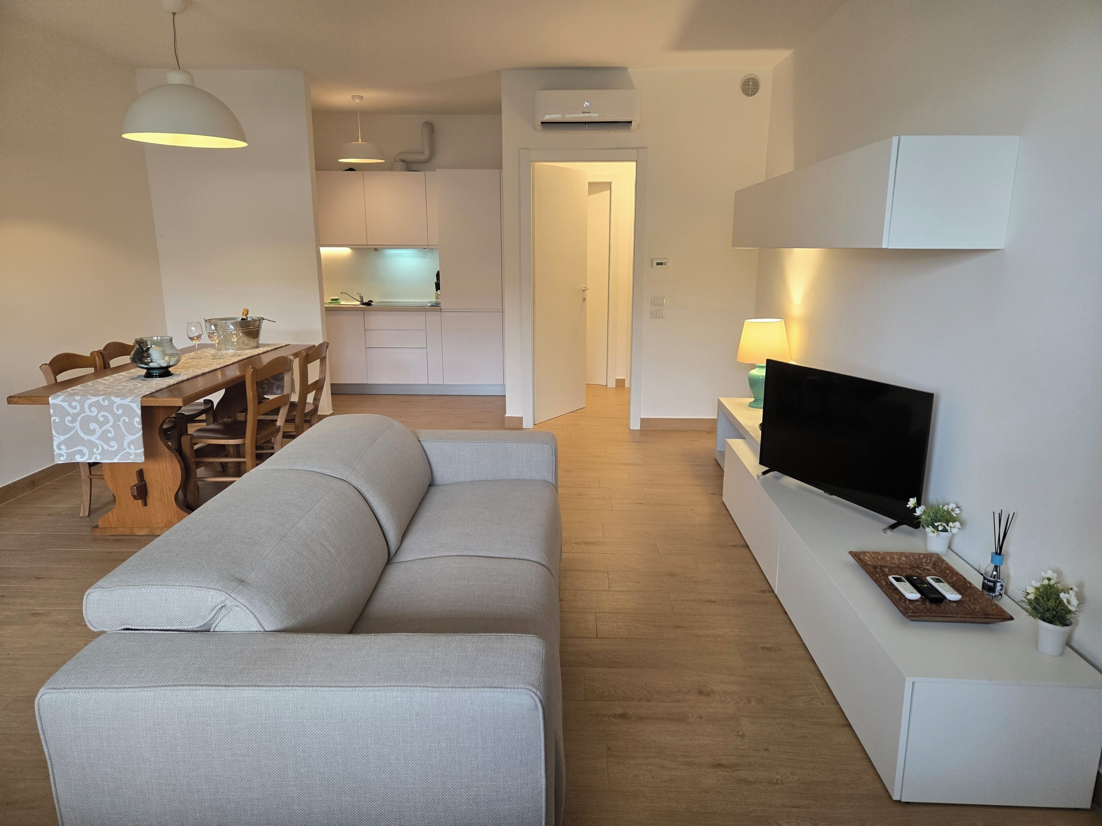 A modern living room with a sofa, dining table, kitchen in the background, and a TV on a stand.