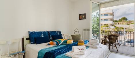A hotel room with a bed, a chair, a table, and a balcony with a view.