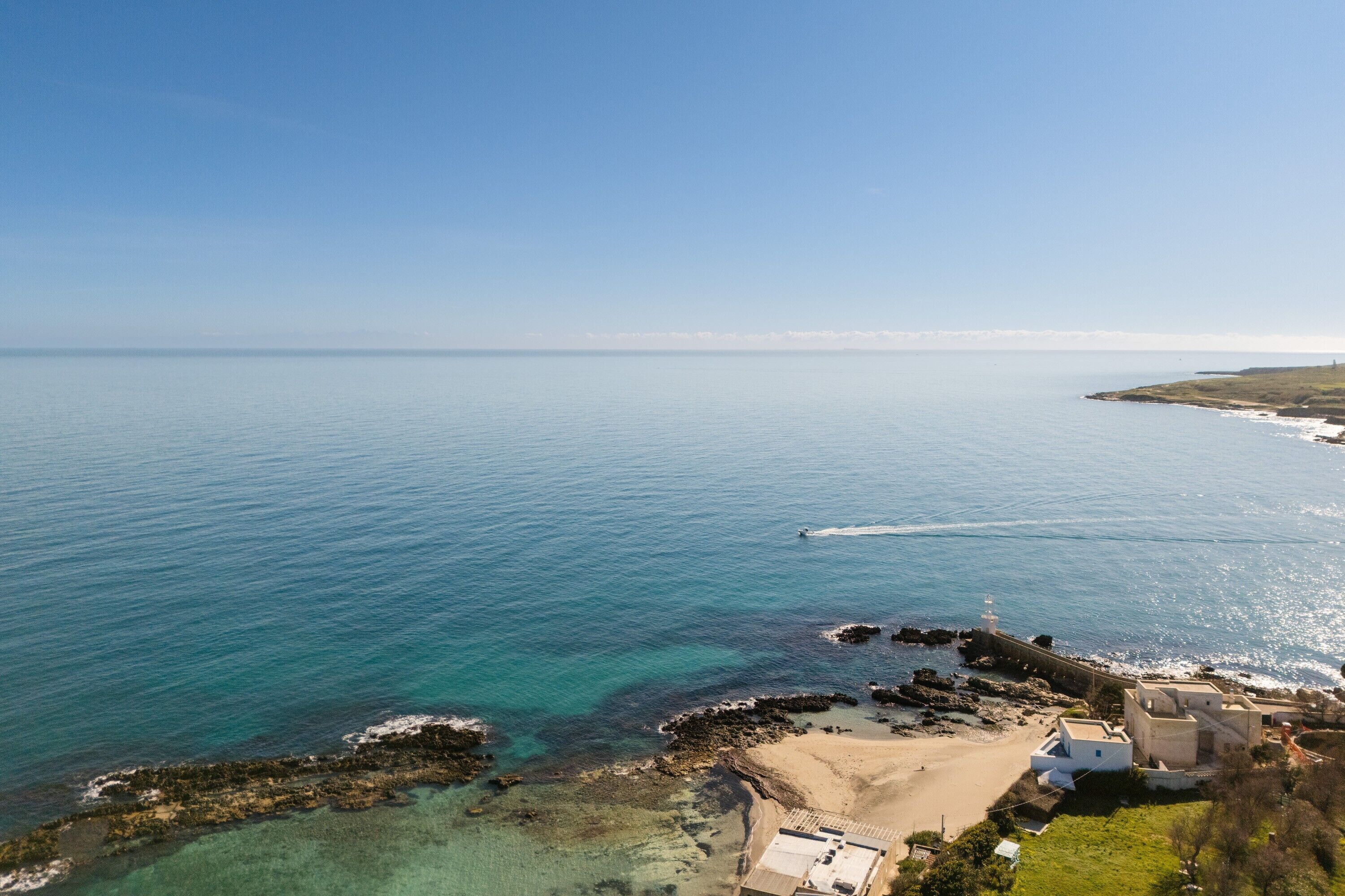 Vista aérea de una zona costera con aguas cristalinas, una playa de arena y un faro.