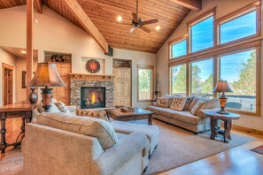 A spacious living room with a fireplace, wooden ceiling, and large windows. - Luxury Retreat with Hot Tub, SHARC, A/C and Bikes (Sunriver)