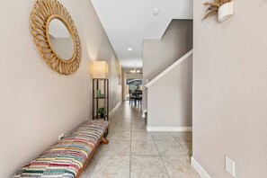 A hallway with a bench, a wall-mounted mirror, a lamp, and a staircase. - 4BR Townhome•Pvt pool•Near theme parks (Kissimmee)
