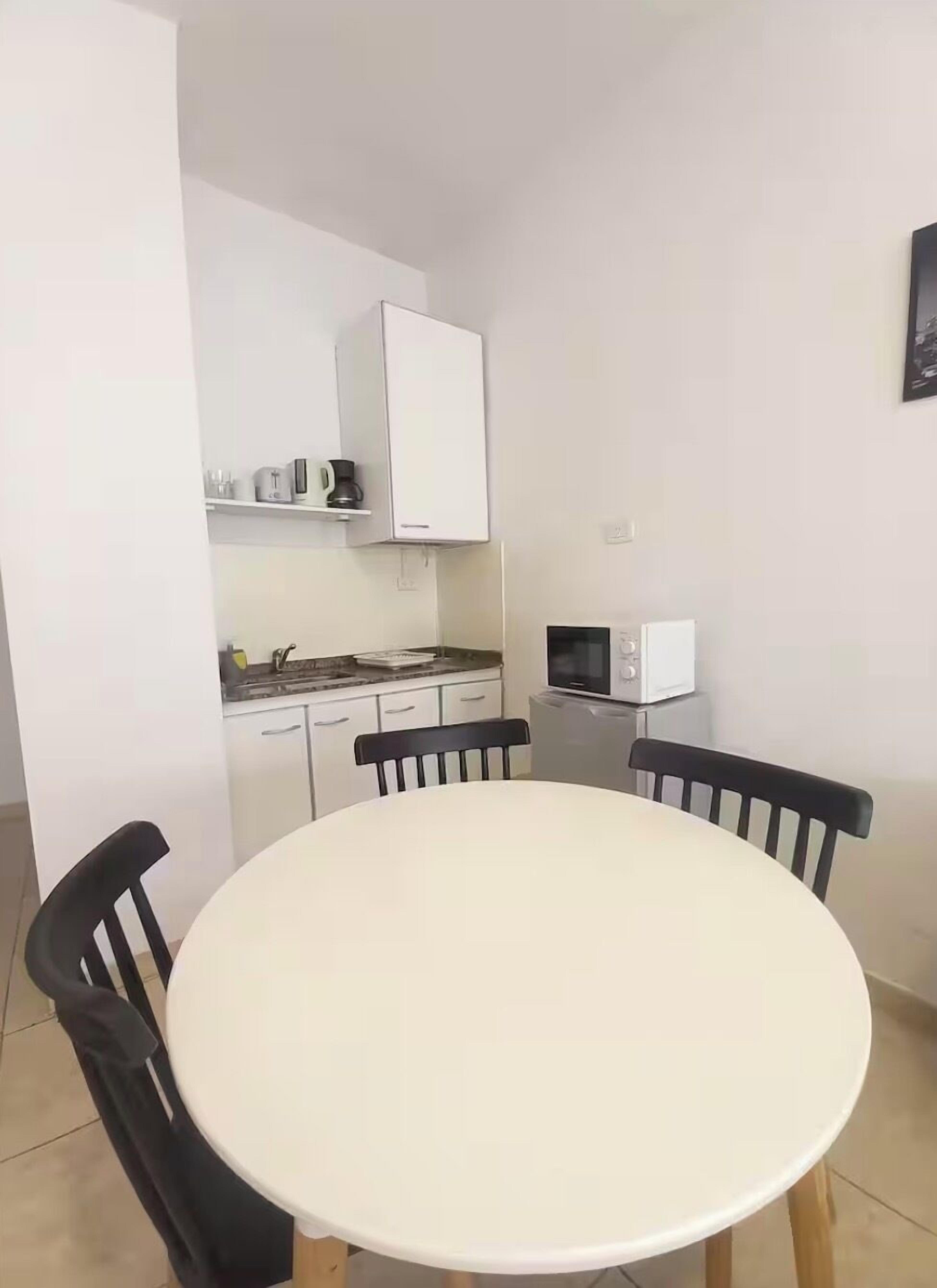 Une cuisine compacte avec des meubles blancs, un four à micro-ondes et un petit plan de travail. On y trouve une table ronde et quatre chaises.