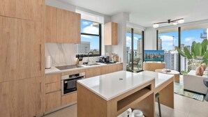 Une cuisine moderne avec des meubles en bois, un plan de travail blanc et une vue sur la ville grâce à de grandes fenêtres.