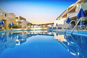 Una piscina con sillones de descanso y sombrillas, un muro de piedra y un edificio con balcones.