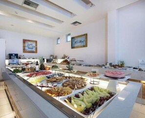 Un bufé con distintos alimentos, un refrigerador y un cuadro en la pared.