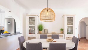 A modern kitchen with a round dining table, grey chairs, and a hanging rattan light fixture. - Villa DOS PALMERAS by Abahana Villas (Calpe)