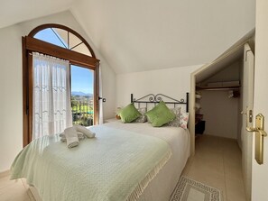 A bedroom with a bed, green pillows, a view through a window, and a door leading to a closet.
