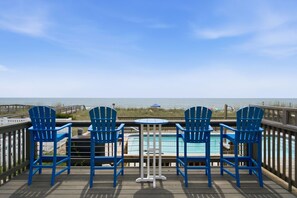 A deck with a pool, blue chairs, and a view of the ocean. - Kure Surf Shack - 5 bed, oceanfront with large pool and elevator (Kure Beach)