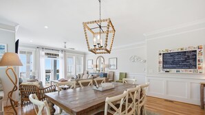 Un coin repas avec une table en bois, des chaises blanches, un lampadaire à pied en fibres tressées et un luminaire décoratif suspendu.