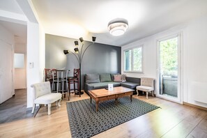 Una sala moderna con sofá, mesa de centro y sillas. Hay una mesa de comedor con sillas, un ventanal grande y una lámpara de techo.