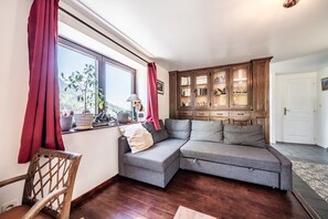 Un soggiorno con un divano modulare grigio, mobili contenitori in legno, una finestra con tende rosse e una sedia di legno.