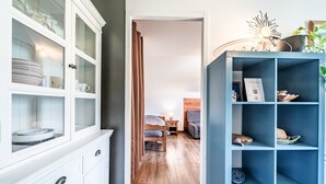Una habitación con piso de madera, una cama con cabecera, una mesita de noche con lámpara y un mueble con puertas de vidrio.