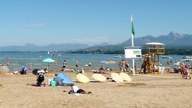 Una playa con sombrillas, una torre de salvavidas y montañas al fondo.