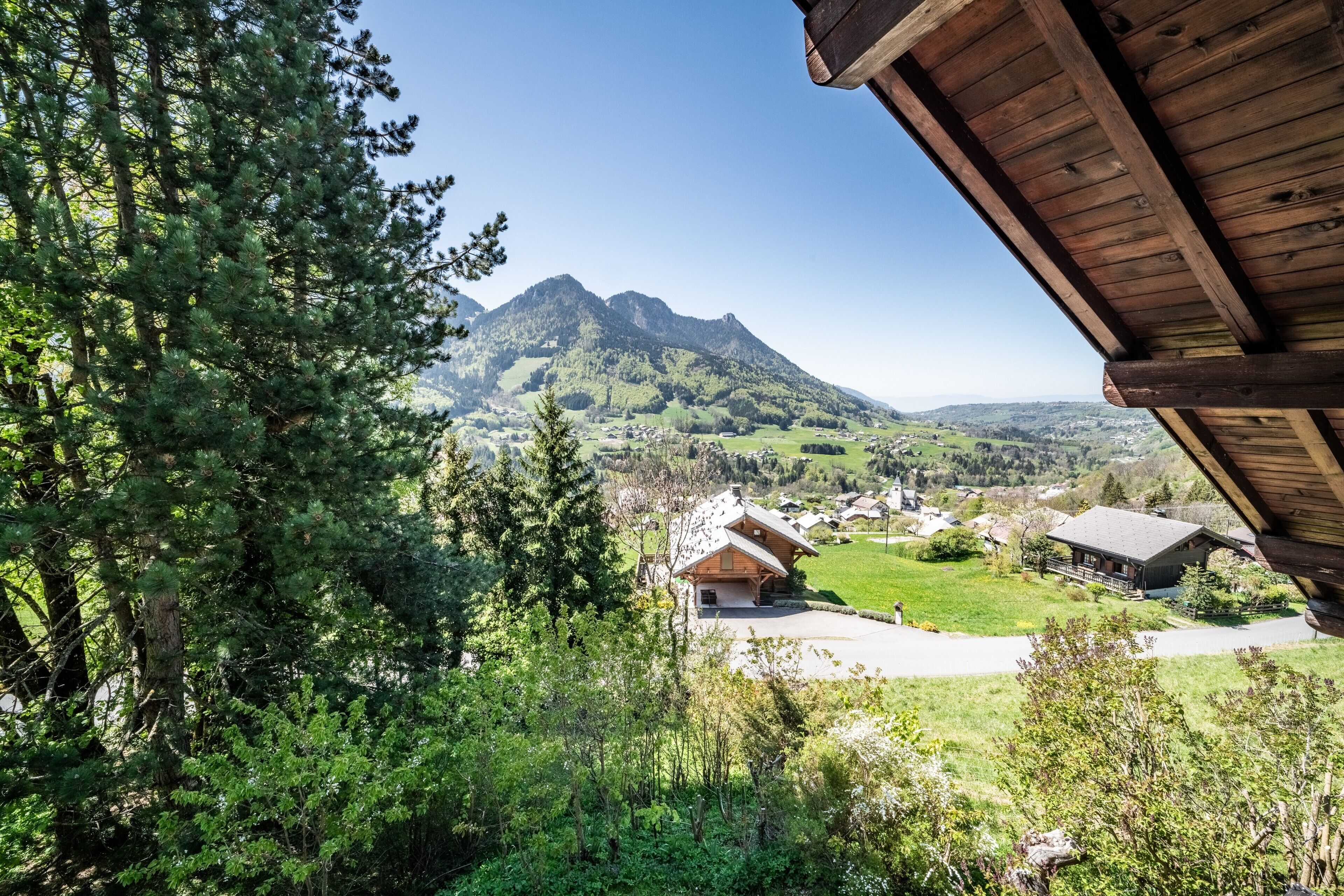 A mountain cabin with a wooden roof, surrounded by lush greenery and a view of a valley.