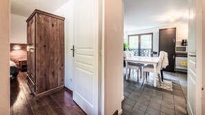 Un pasillo que da a un comedor con una mesa y sillas blancas, una cocina equipada y un armario de madera.