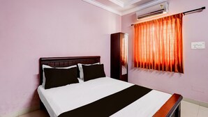 Een hotelkamer met een bed, een airconditioningapparaat, een raam met gordijnen en een lichtschakelaar aan de muur.