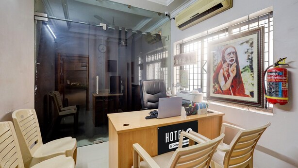 Een hotel receptie met een laptop, stoelen, een brandblusser en een ingelijst beeld aan de muur.