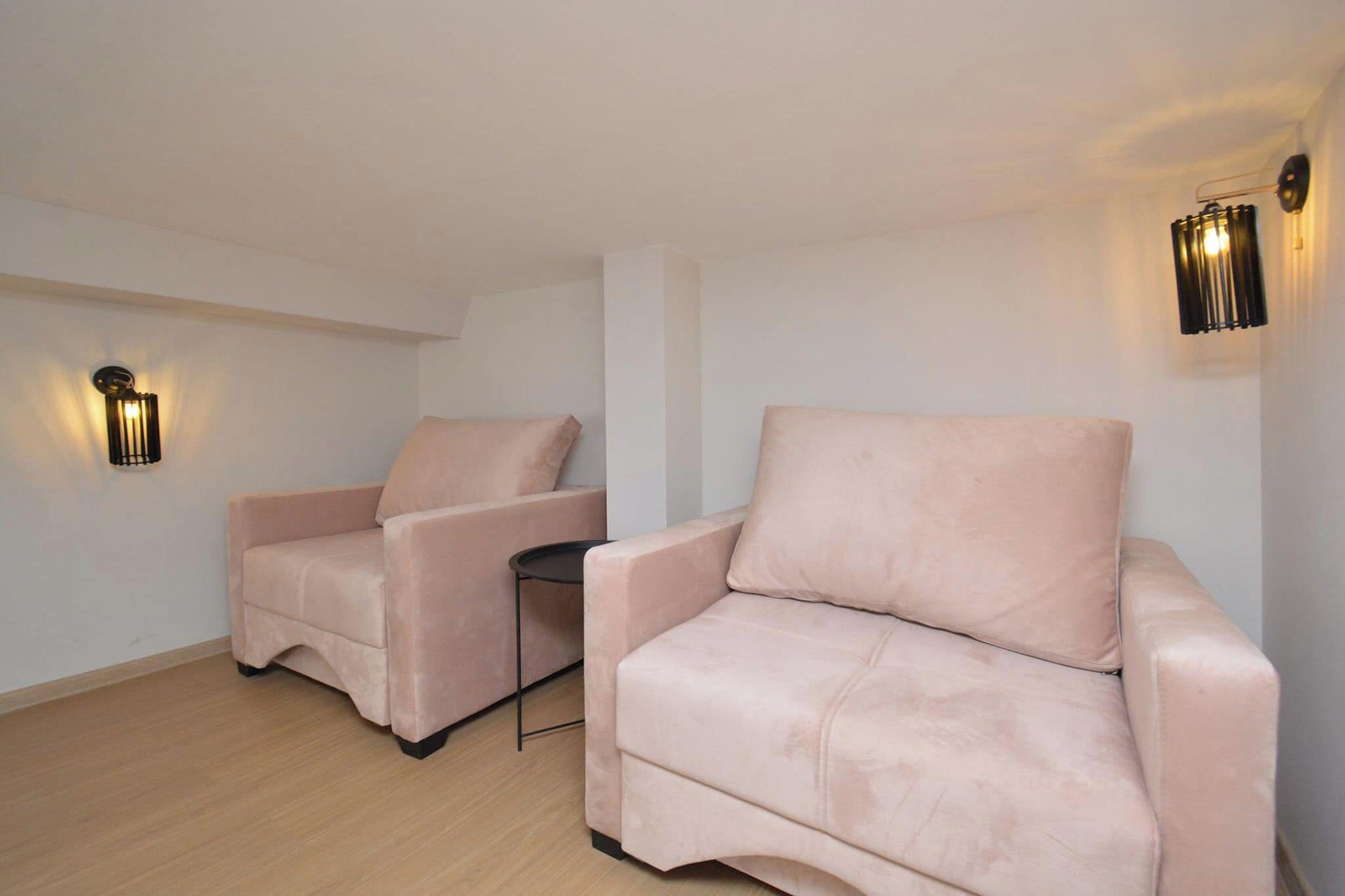 Una habitación con dos sillones color beige y una pequeña mesa, con dos lámparas de pared.