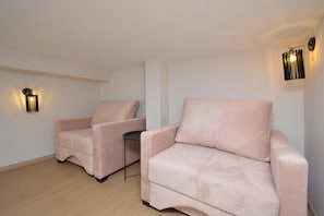 Une pièce avec deux fauteuils beiges et une petite table, ainsi que deux appliques murales.
