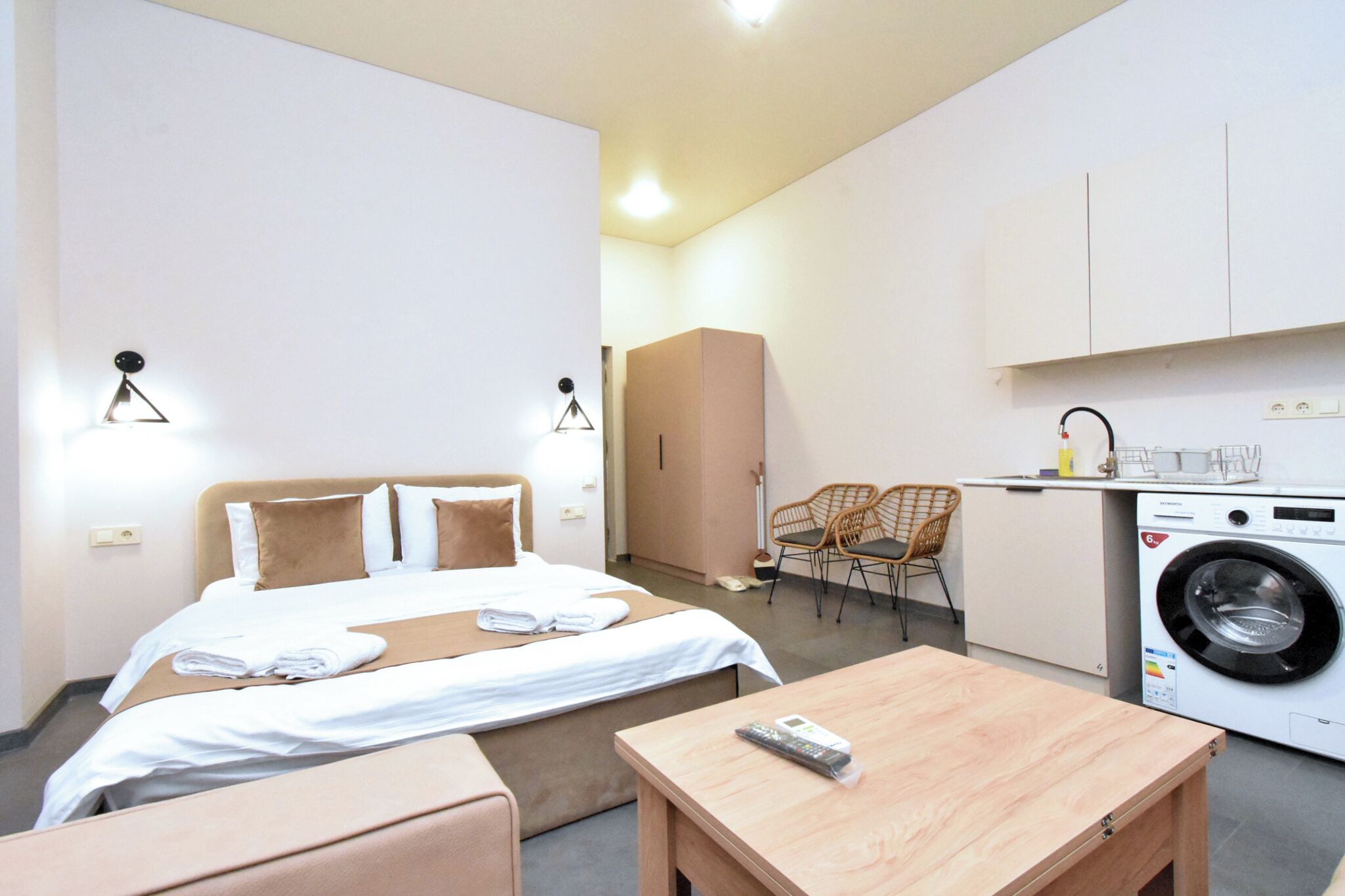 Habitación de hotel con cama, una mesita, una silla, lavadora y kitchenette.