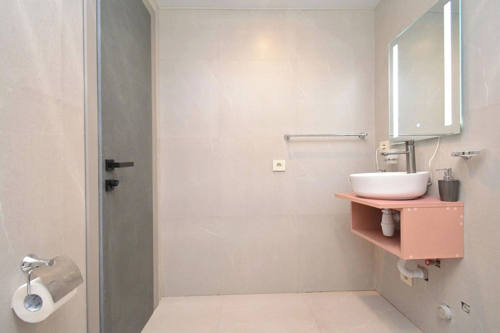 Casa de banho com lavatório branco, espelho e dispensador de toalhas.