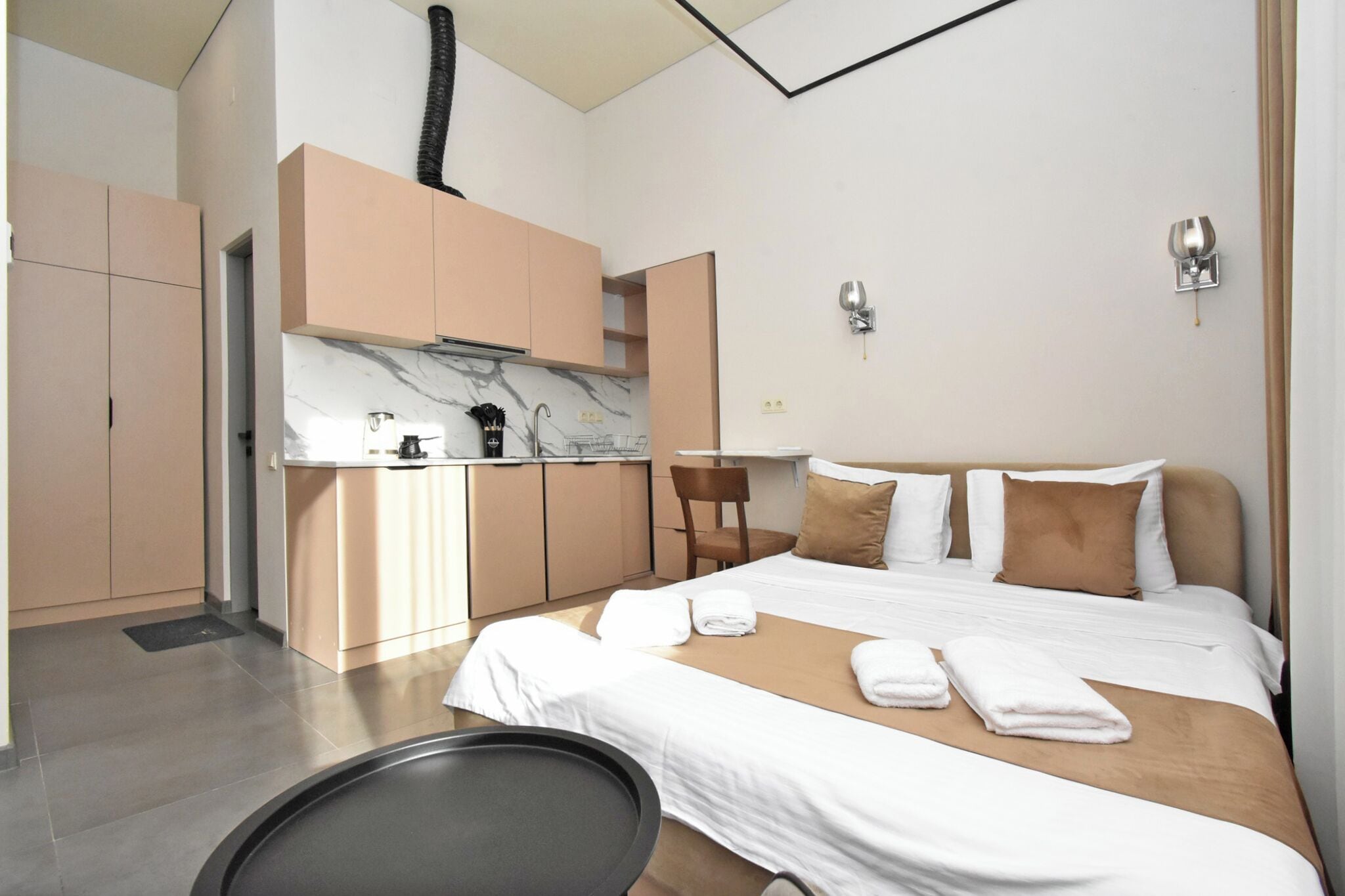 A modern hotel room with a bed, a small kitchenette, and a bathroom.