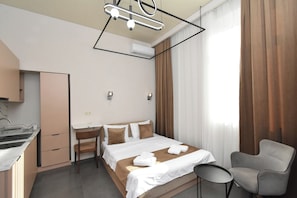 Habitación de hotel con cama, escritorio, silla y lámpara colgante.