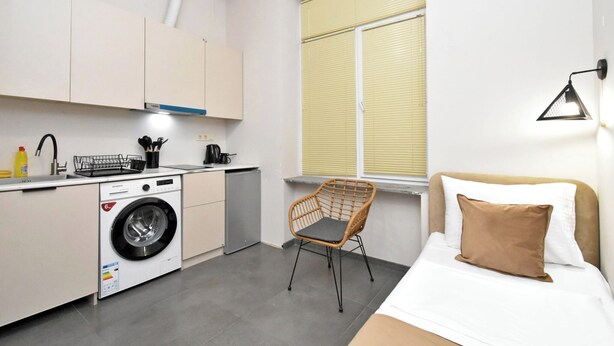 Una habitación de hotel pequeña con una cama, lavadora, una silla y un ventanal con persianas.