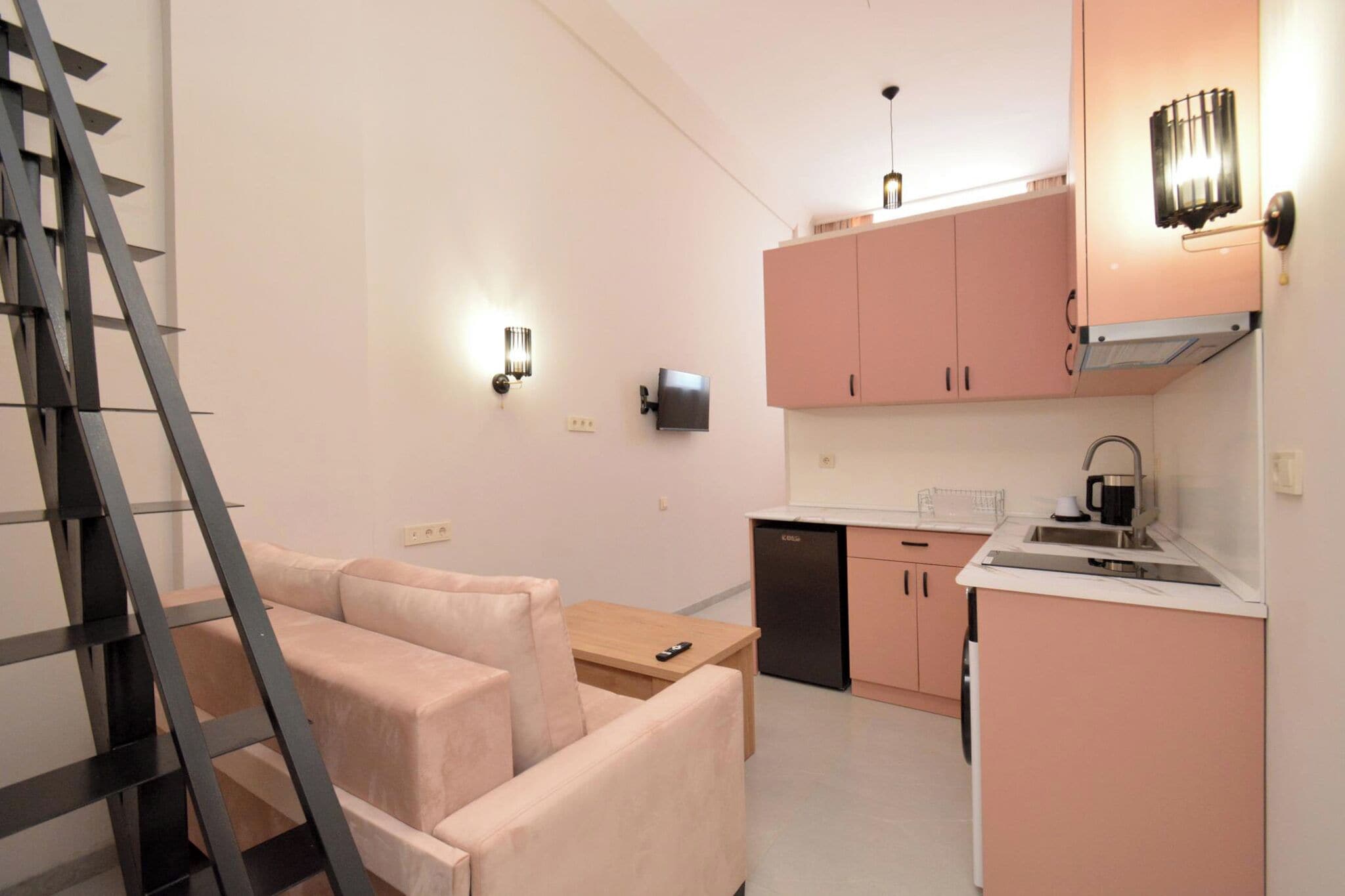 A compact kitchen with pink cabinets, a black refrigerator, and a wooden dining table with two chairs.