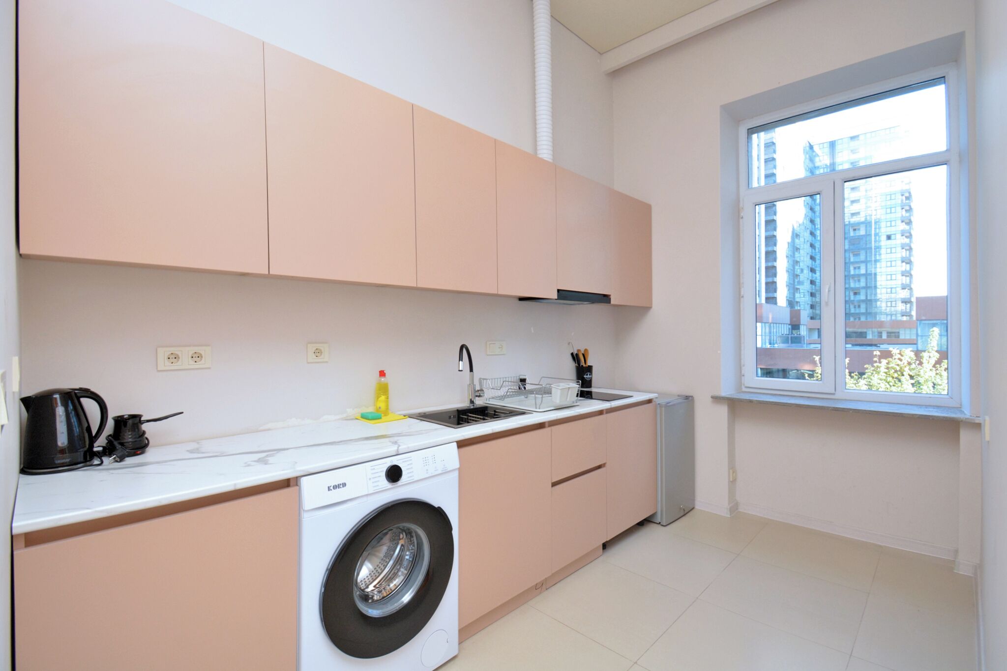 Eine moderne Küche mit Waschmaschine, Wasserkocher und Fenster mit Blick auf Gebäude.