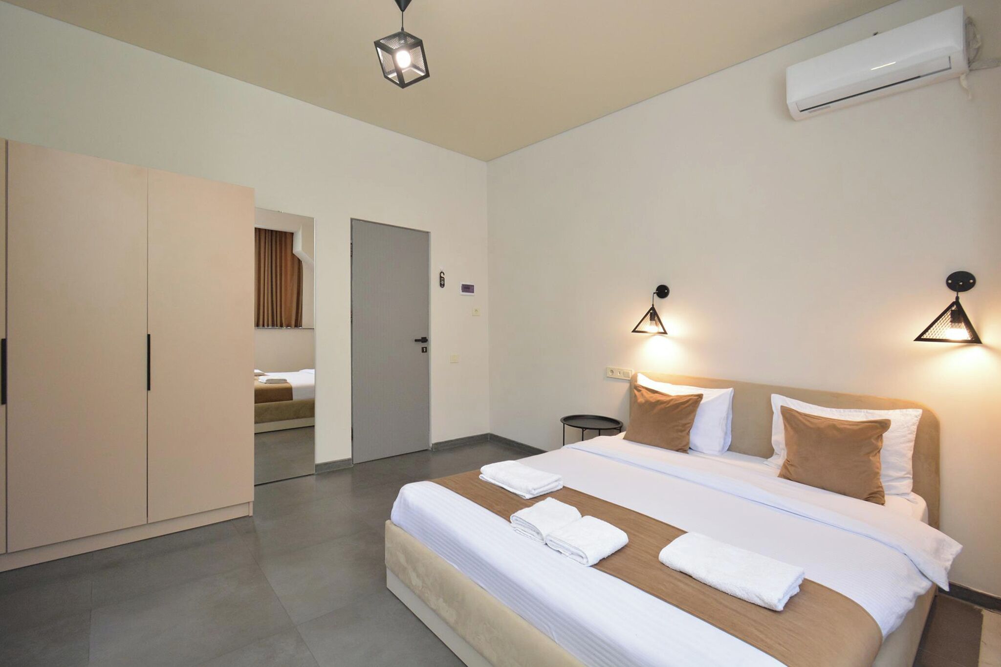 A hotel room with a bed, two bedside lamps, an air conditioning unit, and a wardrobe.
