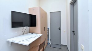 A small room with a flat-screen TV mounted on the wall, a white marble desk, a brown chair, a closed door, and a water dispenser. - Seva Apart-Hotel (Yerevan)