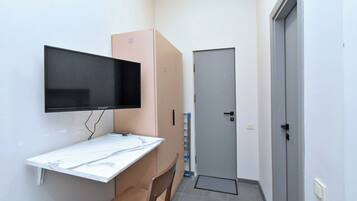 A small room with a flat-screen TV mounted on the wall, a white marble desk, a brown chair, a closed door, and a water dispenser.