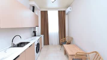 Una cocina compacta con pileta, estufa y lavadora, un comedor con mesa y sillas, y una ventana con cortinas.