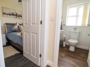 Un dormitorio con cama, almohadas, una mesita de noche y un cuadro de un paisaje urbano en la pared.